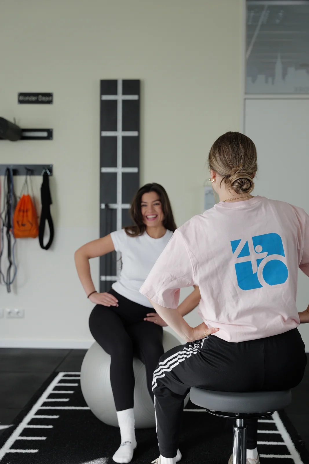 Therapeutin begleitet eine Patientin auf dem Pezziball — Coaching-Moment im Trainingsraum.