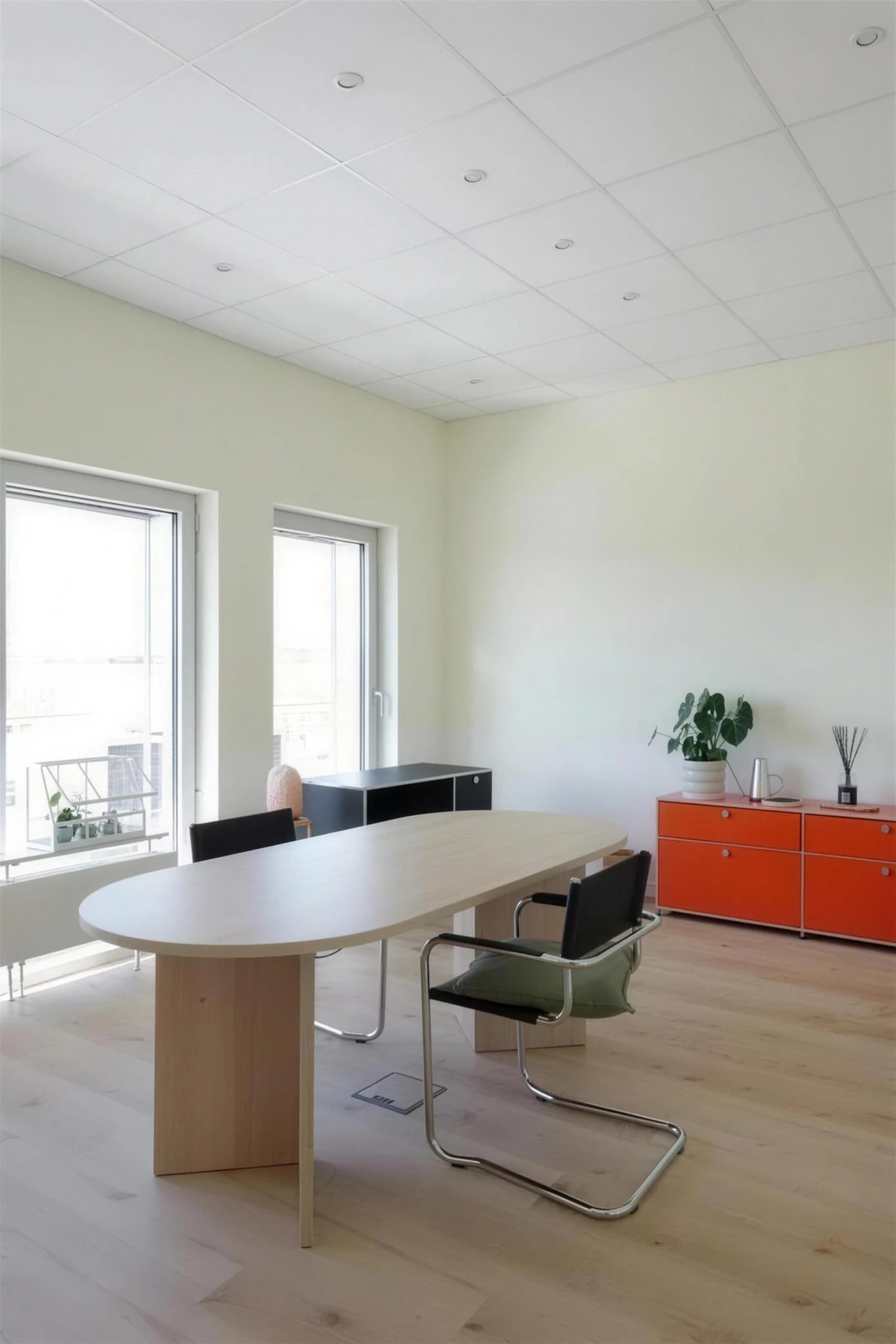 Beratungs­raum mit Holztisch, Stühlen und orangenem USM-Sideboard.