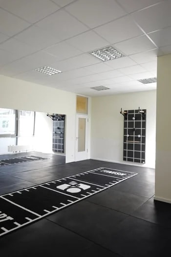 Großer Trainings­raum mit schwarzem Sportboden, Sprossen­gitter und Hyrox-Markierung.