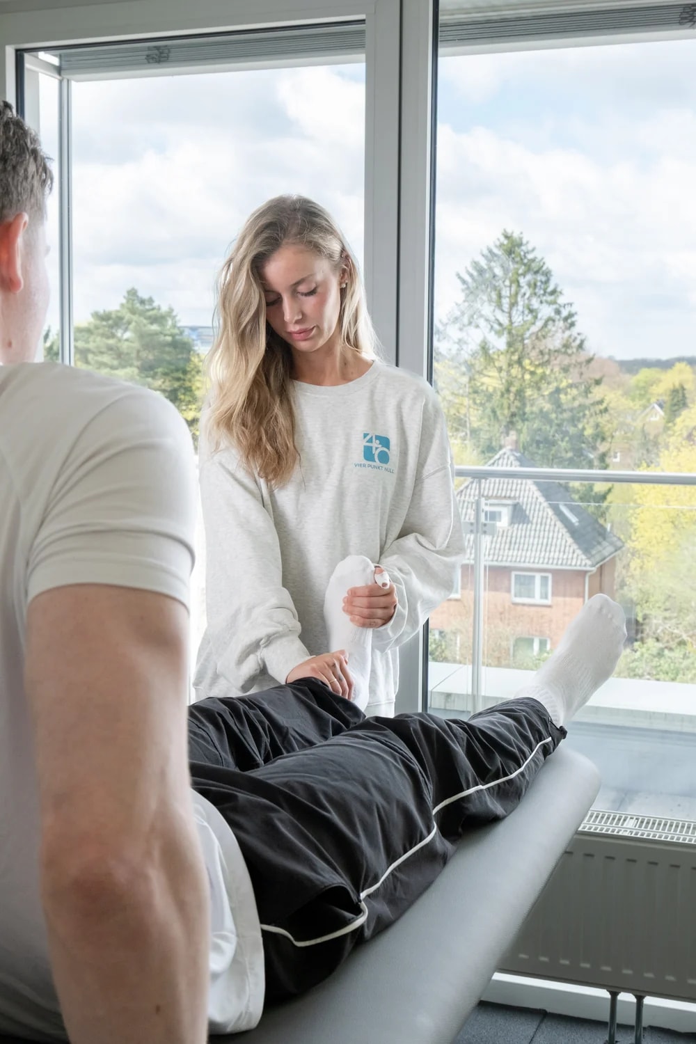 Behandlung eines Beins auf der Therapieliege am Fenster, Tageslicht von draußen.