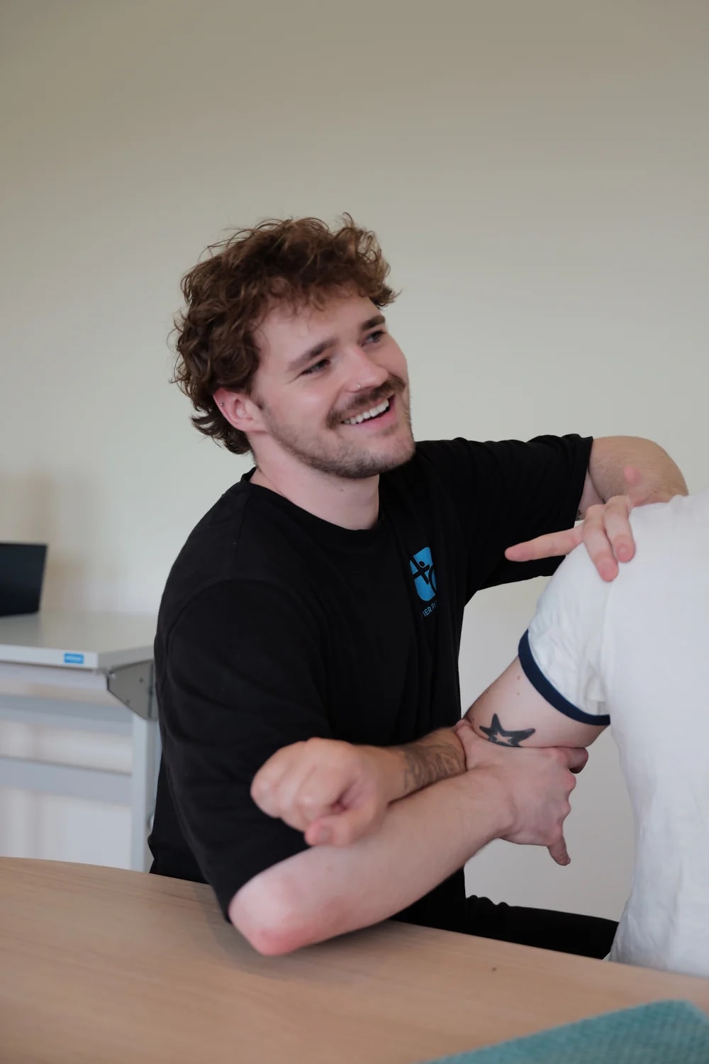 Therapeut bewegt den Arm einer sitzenden Person am Behandlungstisch.