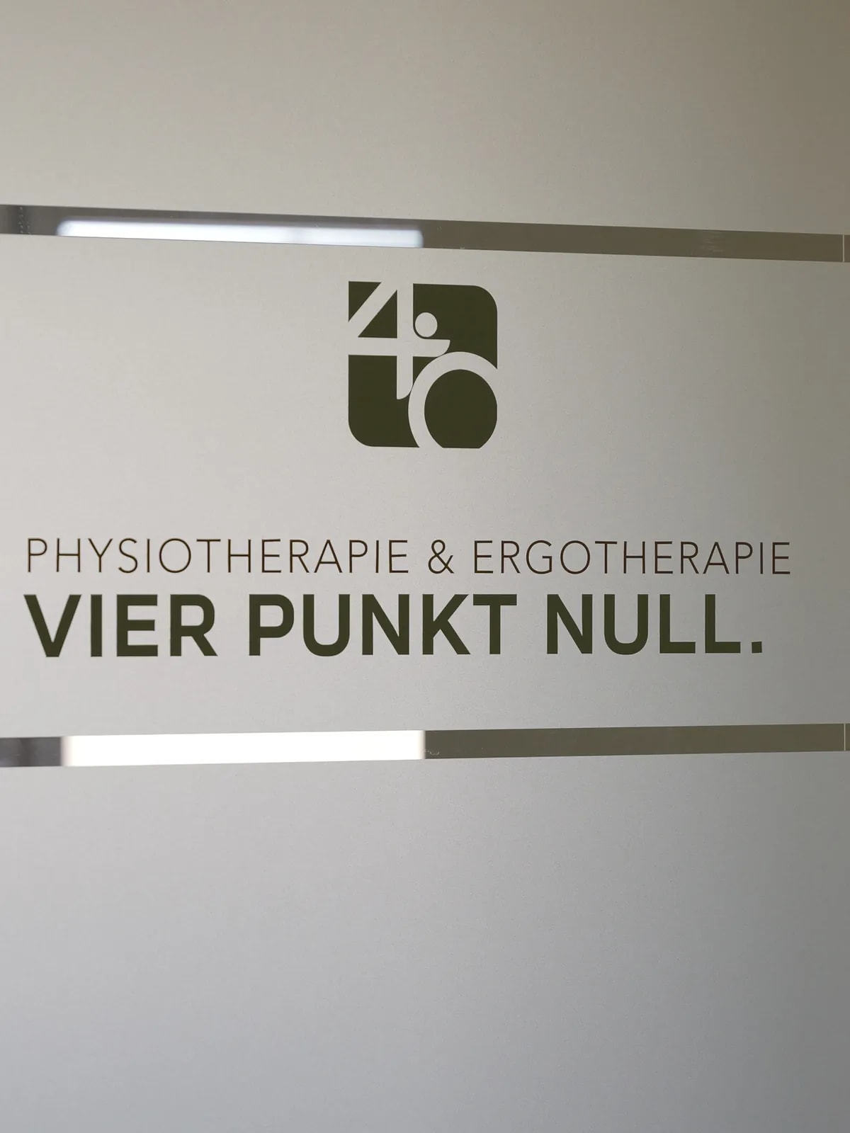 Milchglastür mit dem Praxislogo und dem Schriftzug Physiotherapie & Ergotherapie Vier Punkt Null in Olivgrün.