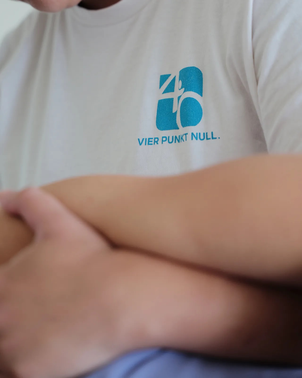 Nahaufnahme: Praxislogo auf einem weißen T-Shirt, davor verschränkte Unterarme.