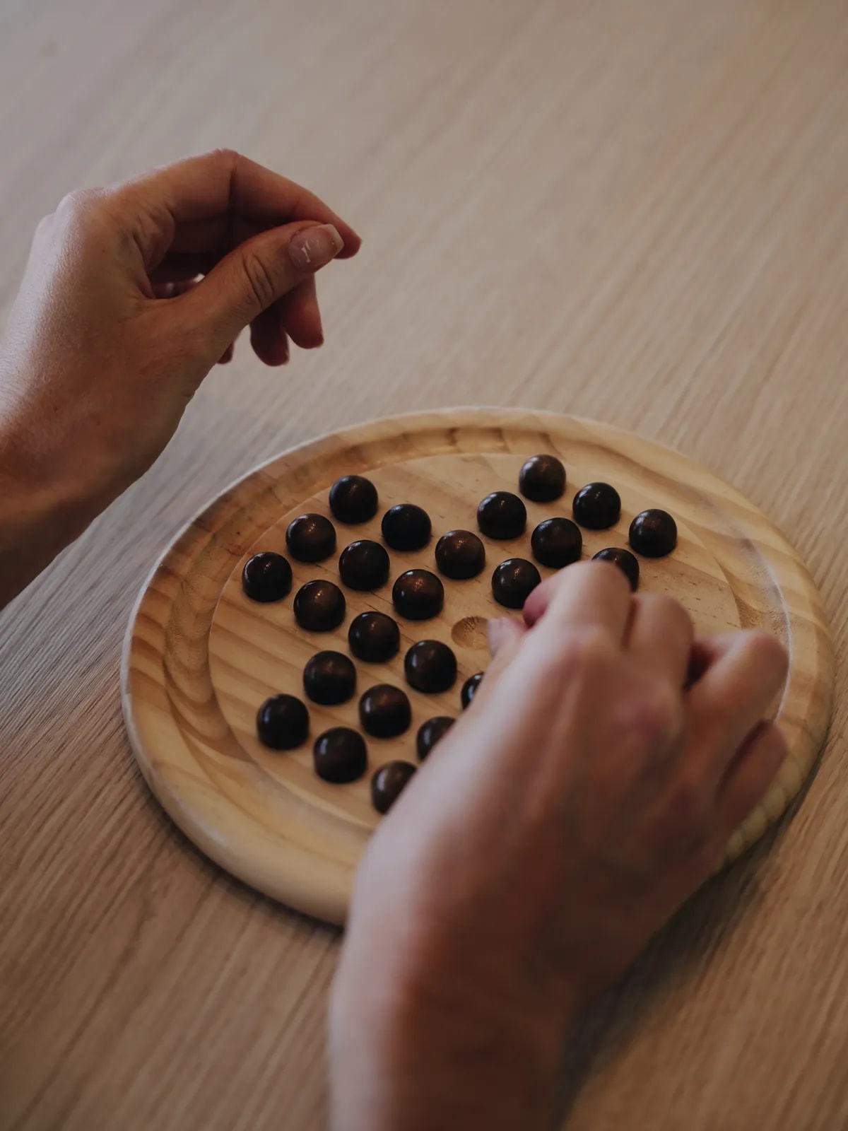 Zwei Hände an einem Brettspiel aus Holz mit dunklen Kugeln auf einem Holztisch.