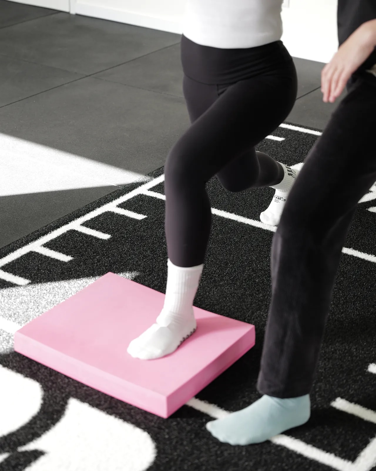 Patientin steht auf einem Bein auf einem rosa Balancekissen, daneben ein Therapeut.
