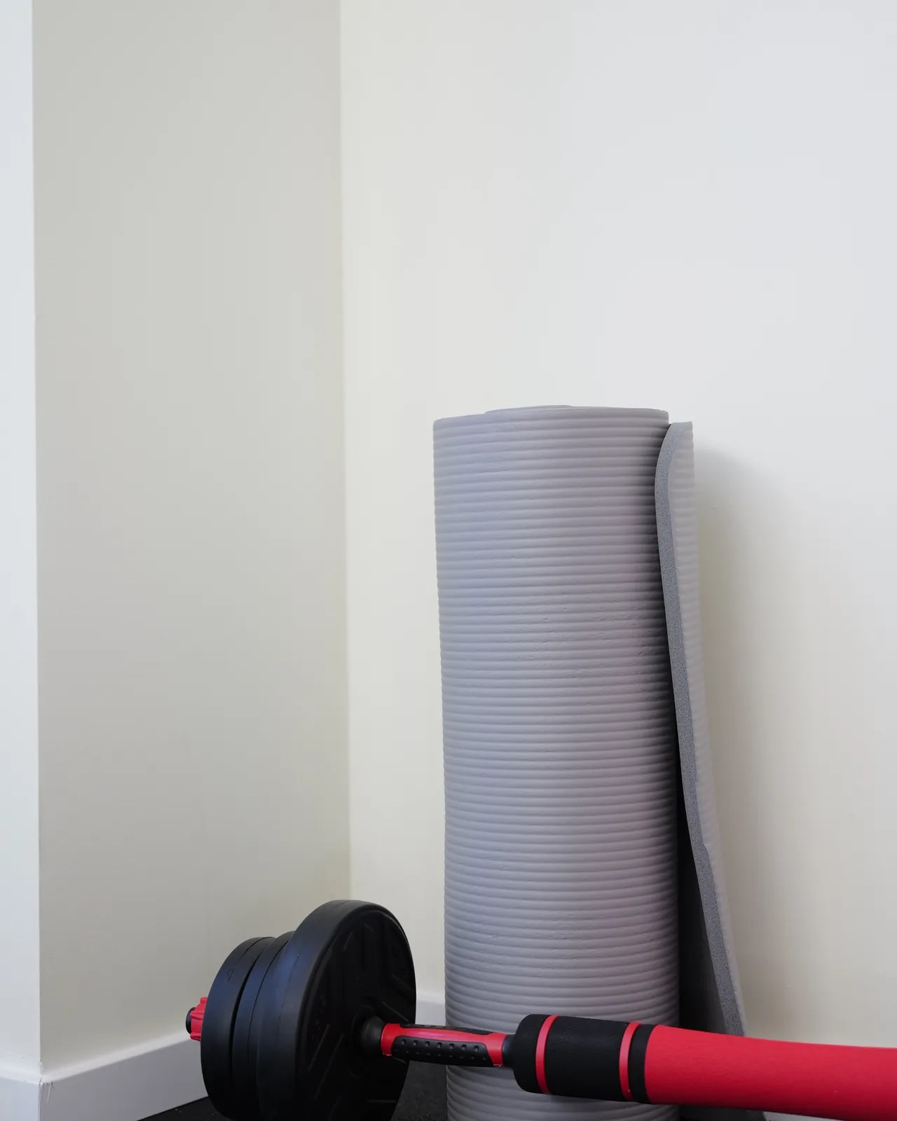 Gerollte Gymnastikmatte und eine Hantel an der Wand.