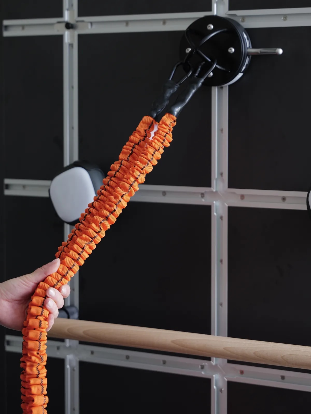 Eine Hand zieht ein orangefarbenes Band an der schwarzen Trainingswand.