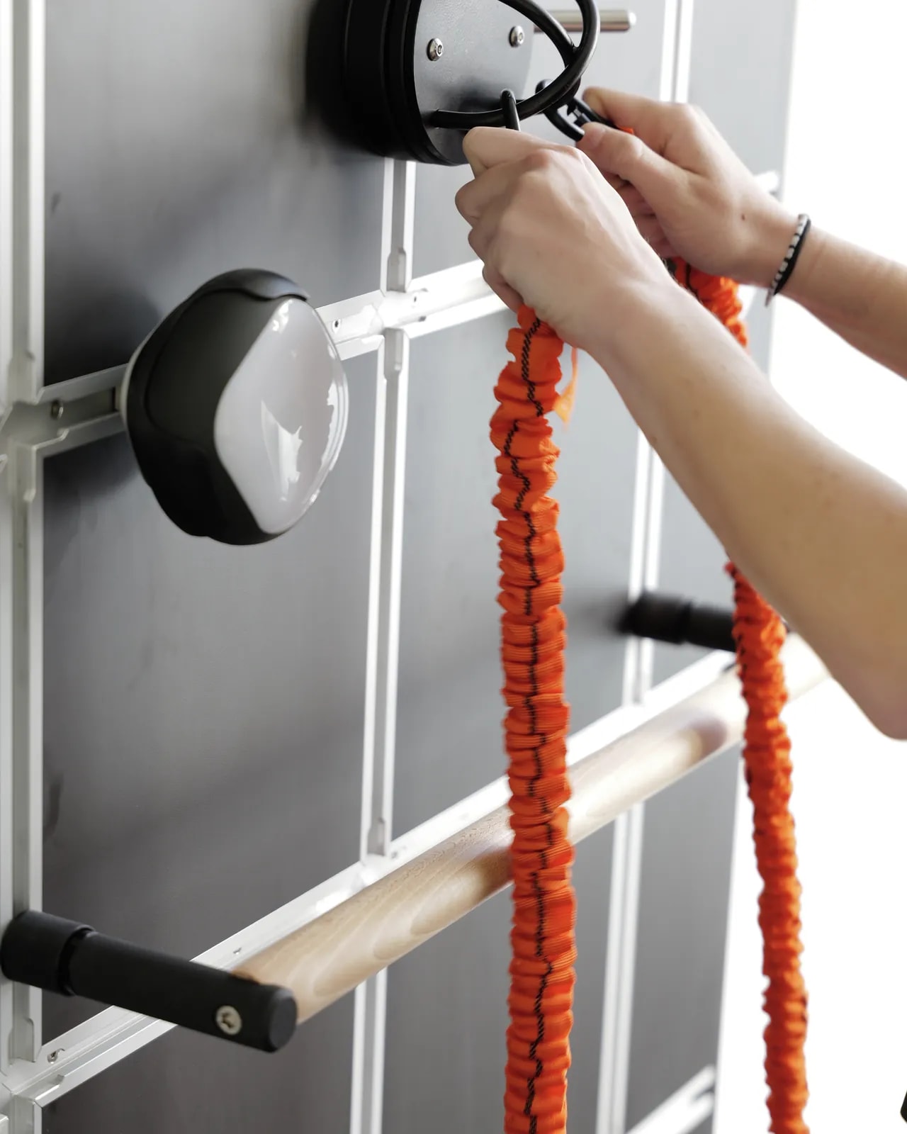 Hände hängen orangefarbene Bänder in die Trainingswand ein.