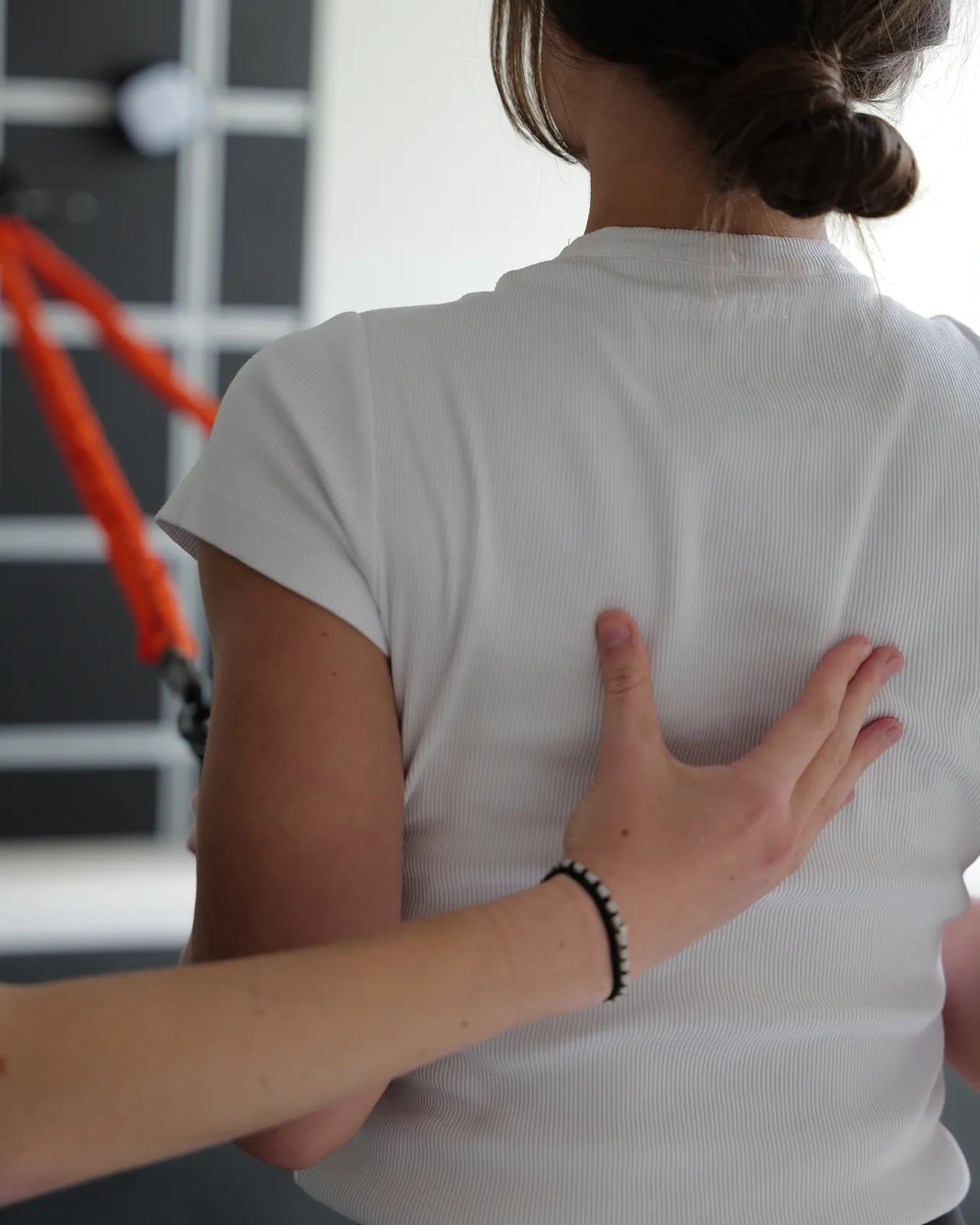 Hand einer Therapeutin am Schulterblatt einer Patientin, die an einem Band zieht.