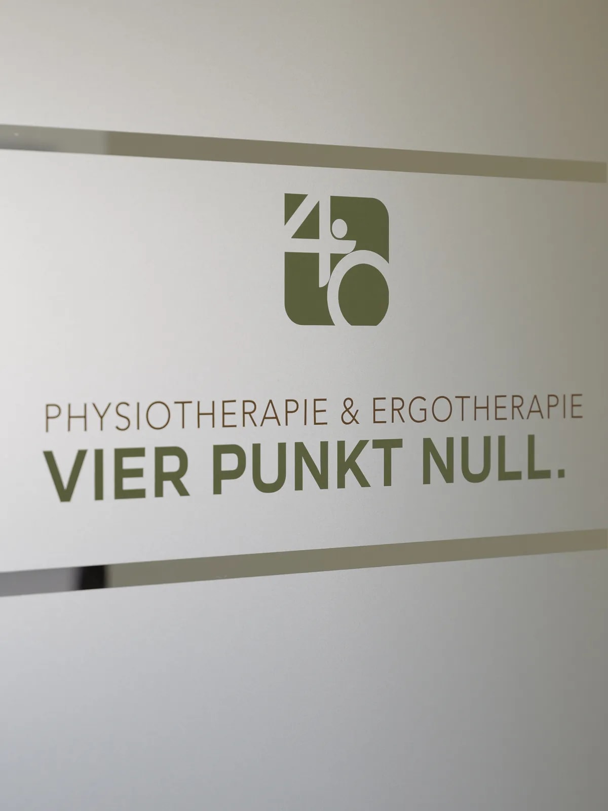 Milchglastür mit dem Praxislogo und dem Schriftzug Physiotherapie & Ergotherapie VIER PUNKT NULL.