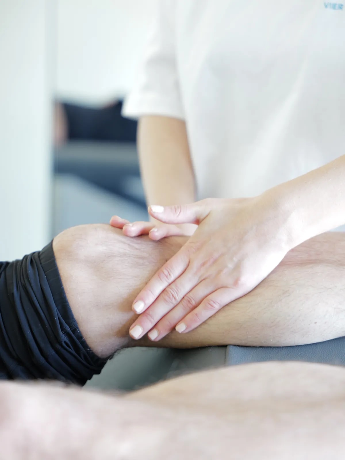 Zwei Hände liegen flach auf Knie und Unterschenkel einer liegenden Person.