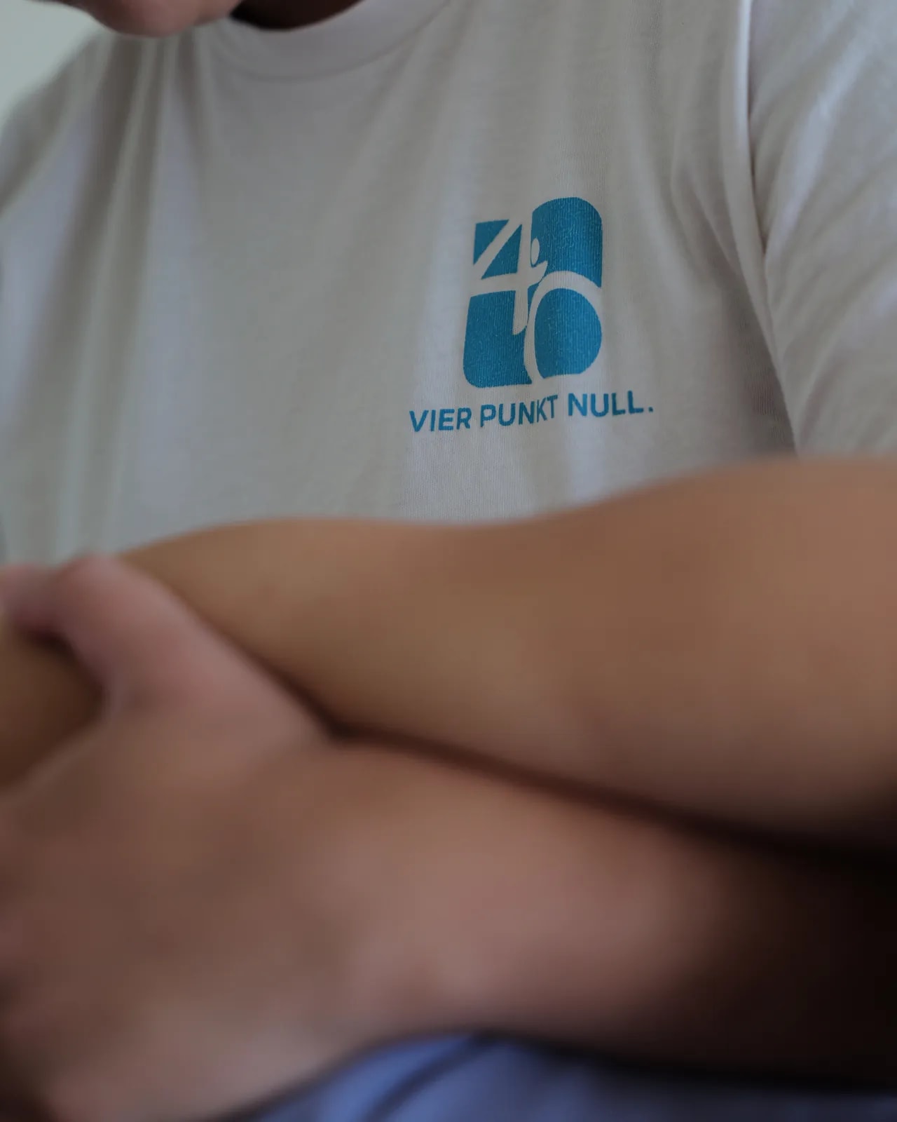 Nahaufnahme: Praxislogo auf einem weißen T-Shirt, davor unscharf verschränkte Unterarme.