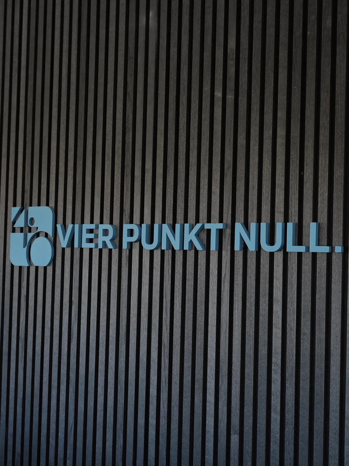 Holzlamellen-Wand am Empfang mit dem Schriftzug VIER PUNKT NULL.