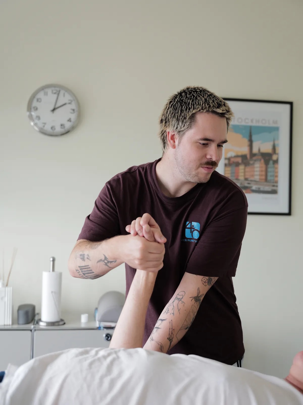 Therapeut hält den senkrecht gestreckten Arm eines liegenden Patienten am Handgelenk.