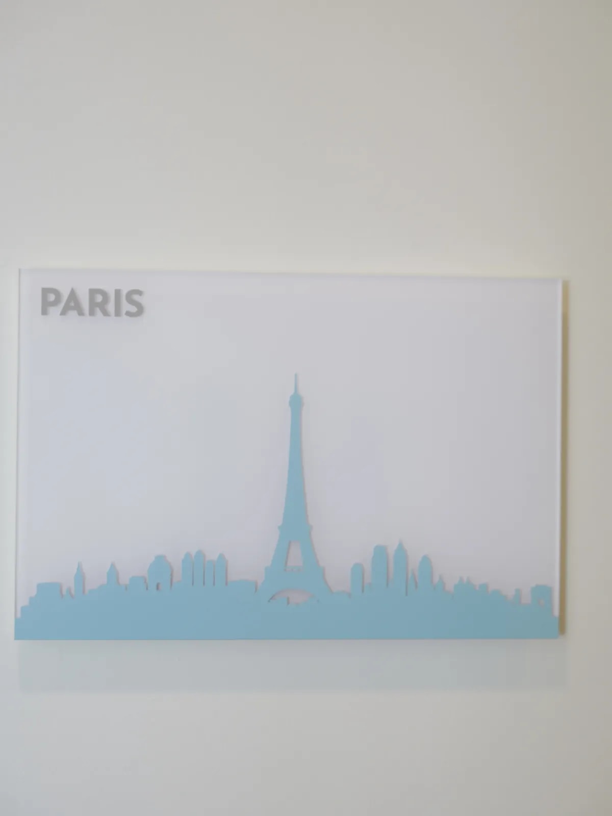 Raumschild mit der Aufschrift PARIS und der Silhouette des Eiffelturms an einer hellen Wand.