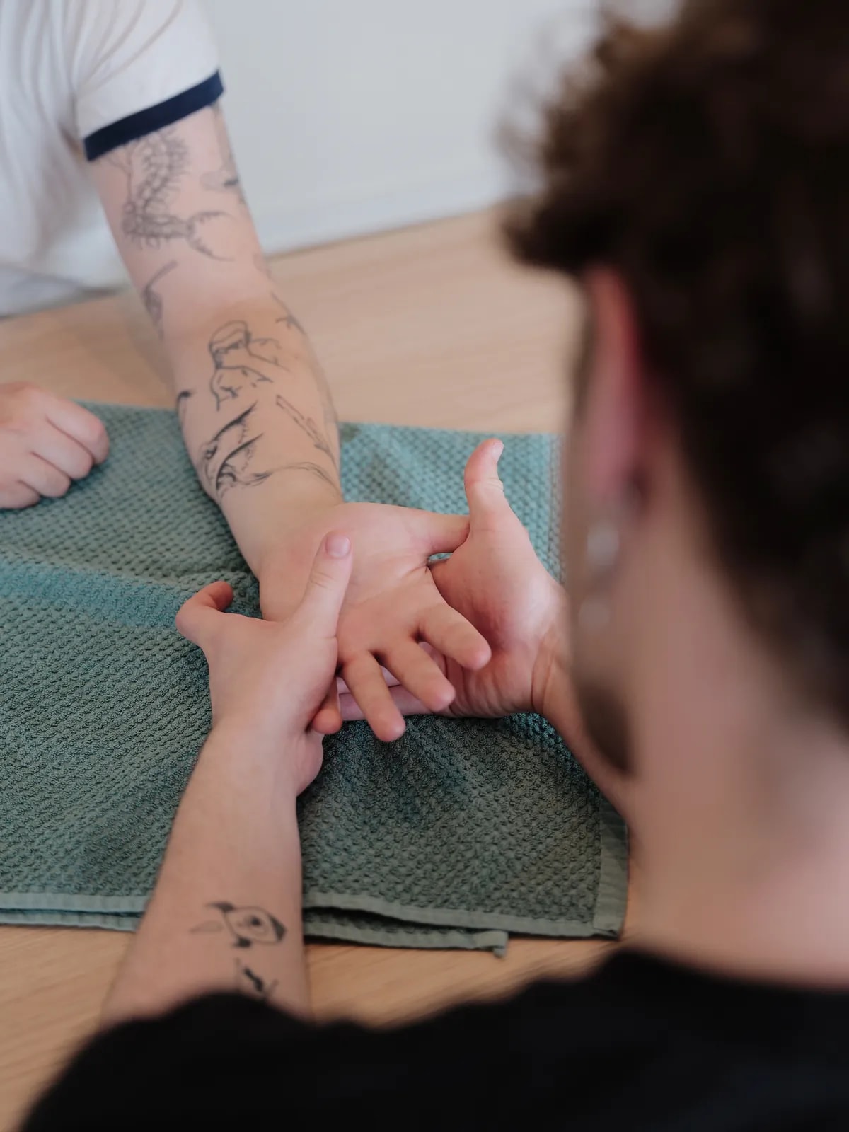 Therapeut hält Hand und Handgelenk eines Patienten, die auf einem Handtuch liegen, Blick über seine Schulter.