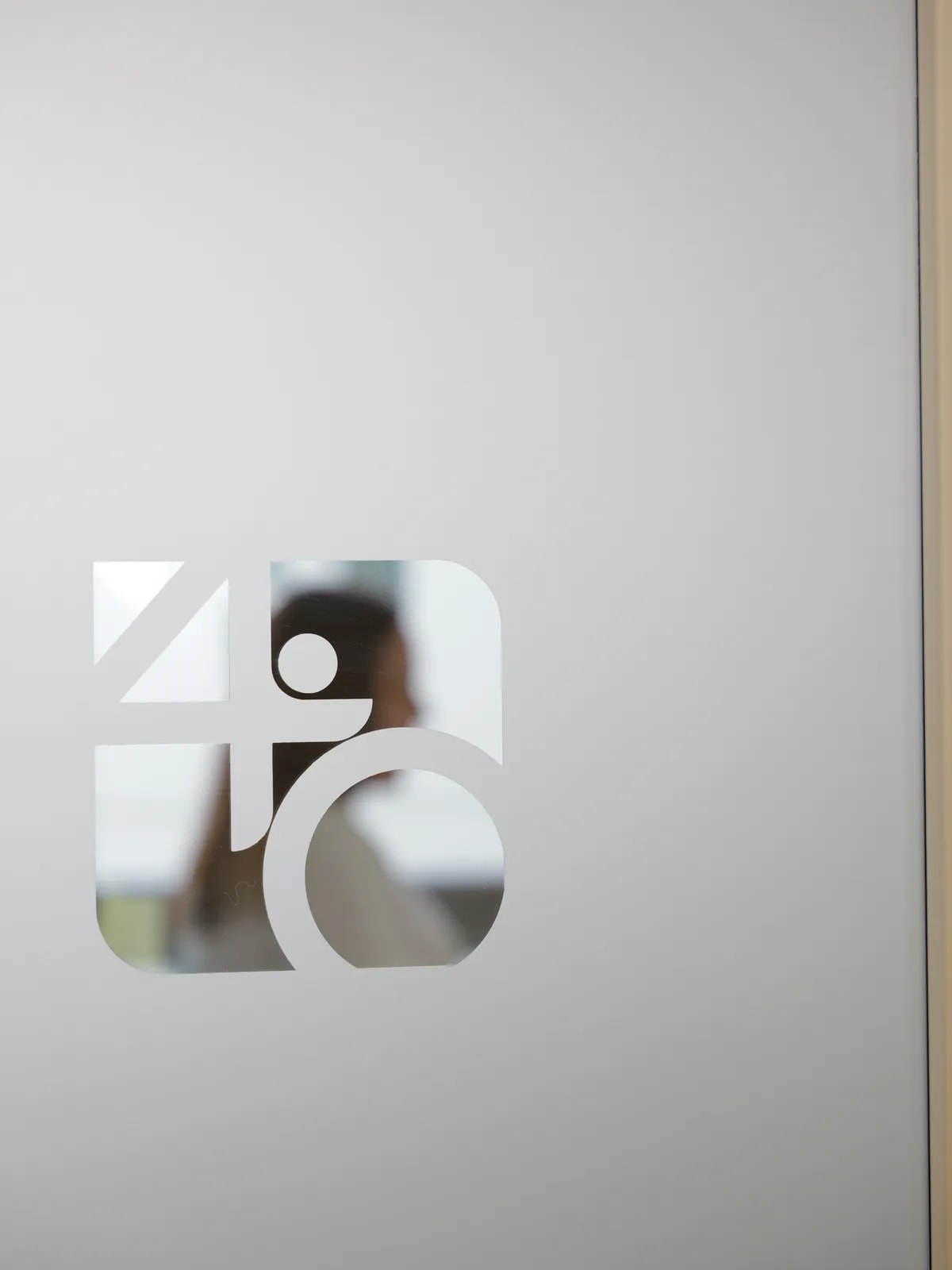 Milchglastür mit ausgeschnittenem Logo, durch das eine Person unscharf zu erkennen ist.