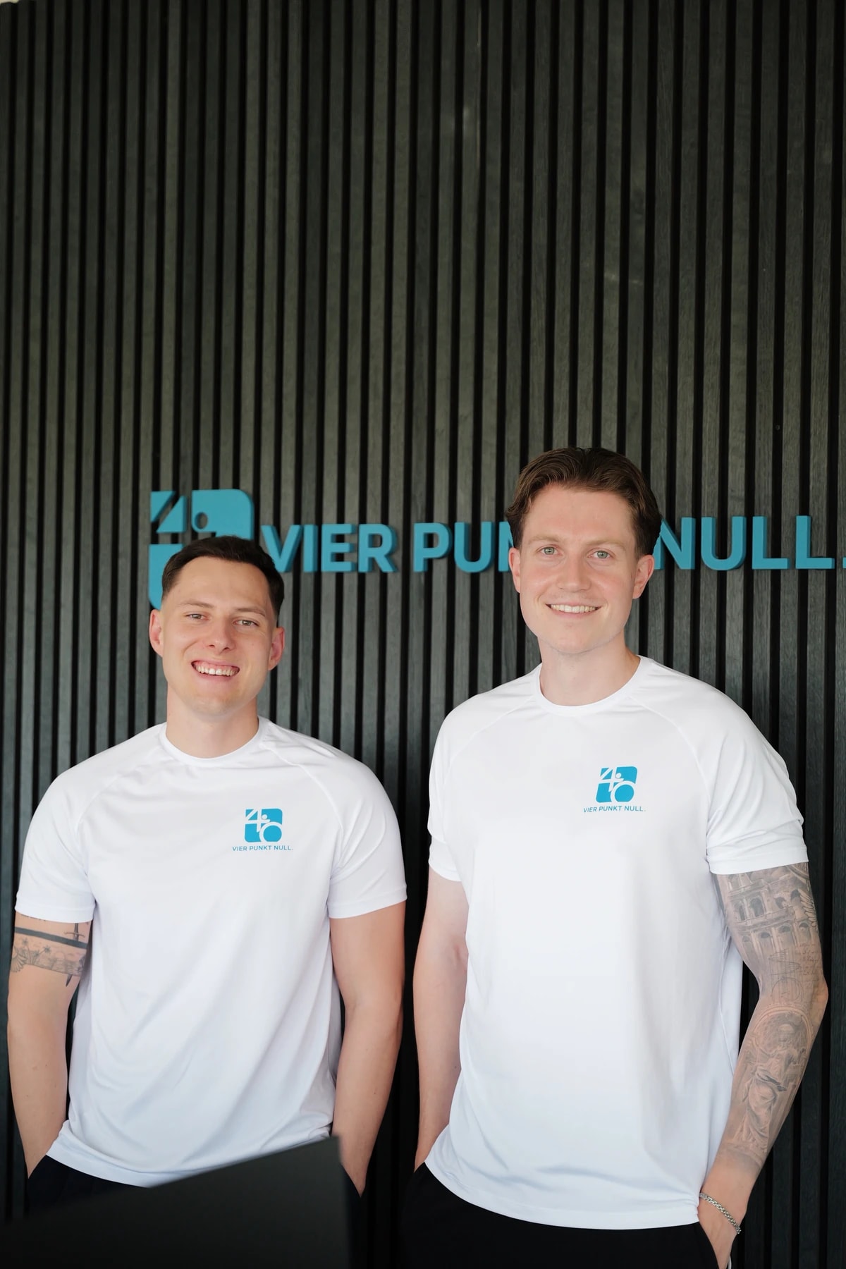 Nick Enghardt und Marvin Eberhards, Gründer der Praxis Vier Punkt Null, vor der Praxiswand mit dem Vier-Punkt-Null-Schriftzug.