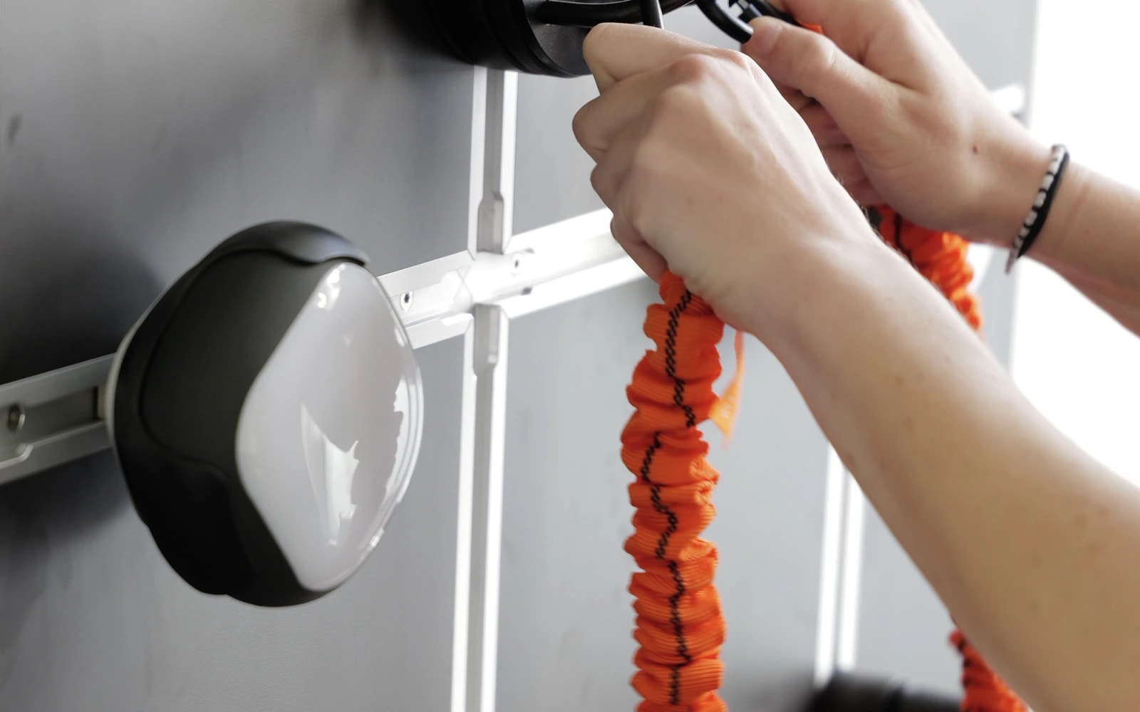 Hände hängen ein Zugband in eine Trainingswand ein.
