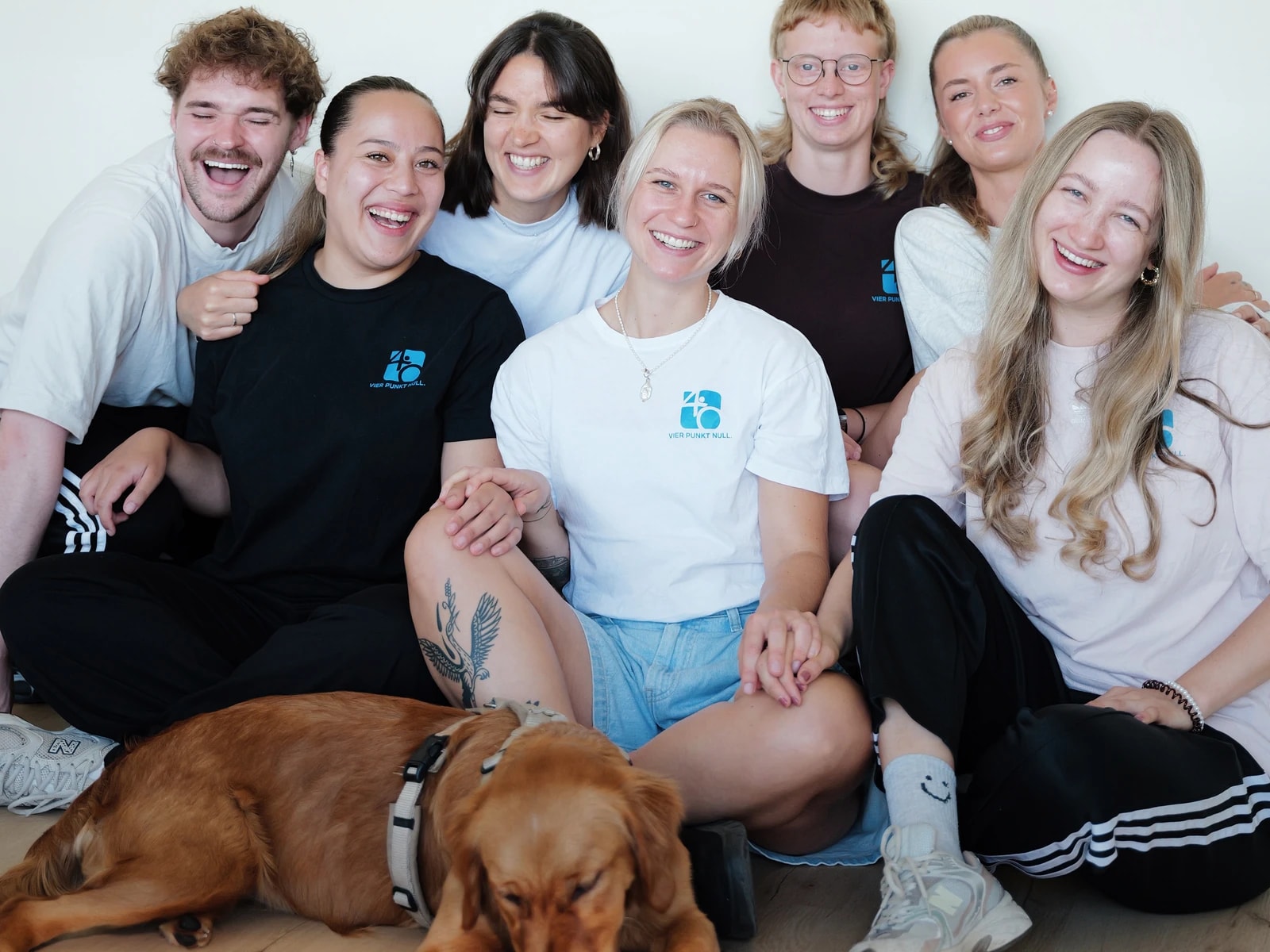 Ein Teil des Teams sitzt zusammen mit dem Praxishund auf dem Boden und lacht.